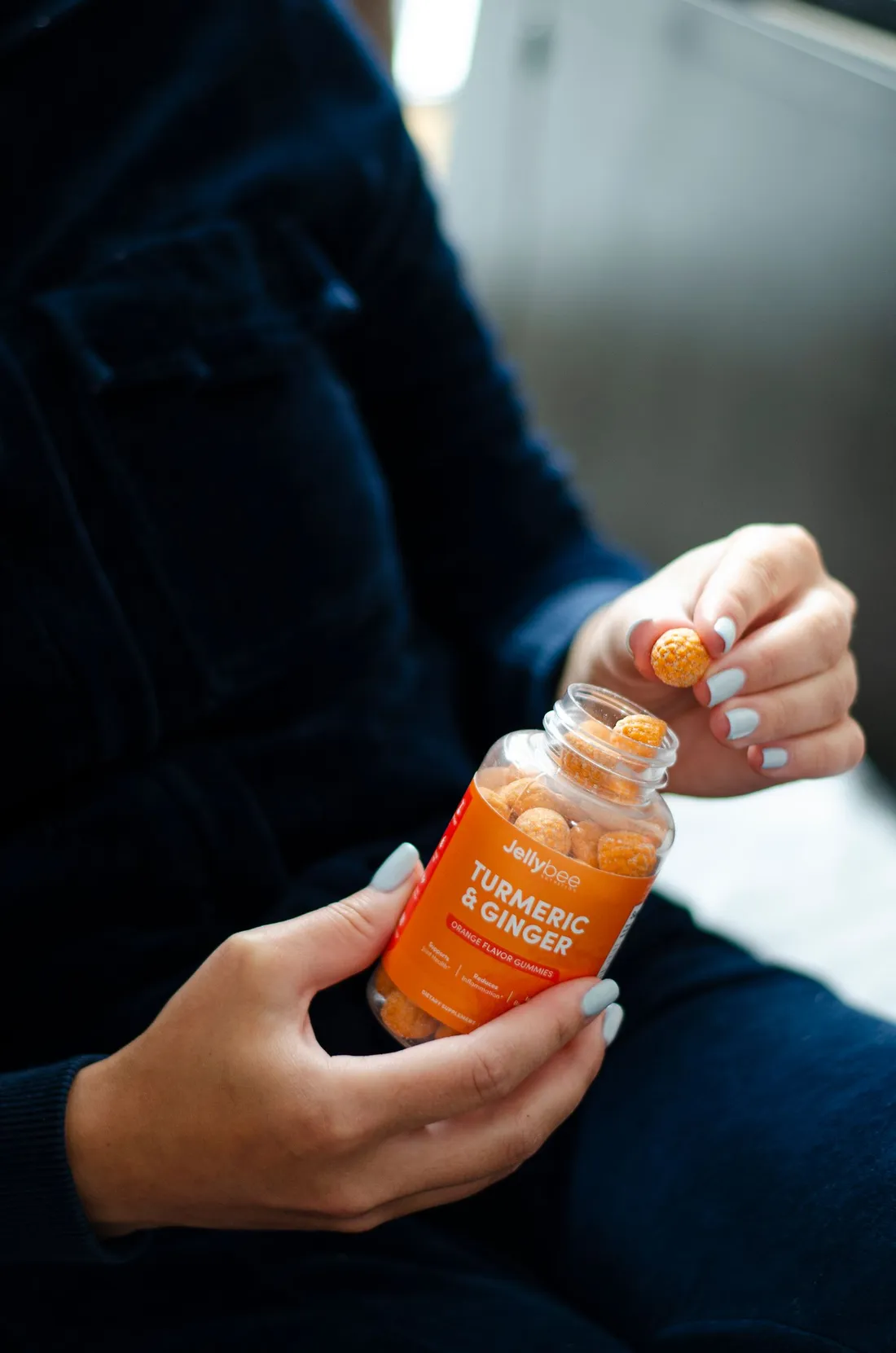 A hand holding an orange plastic gummy bottle