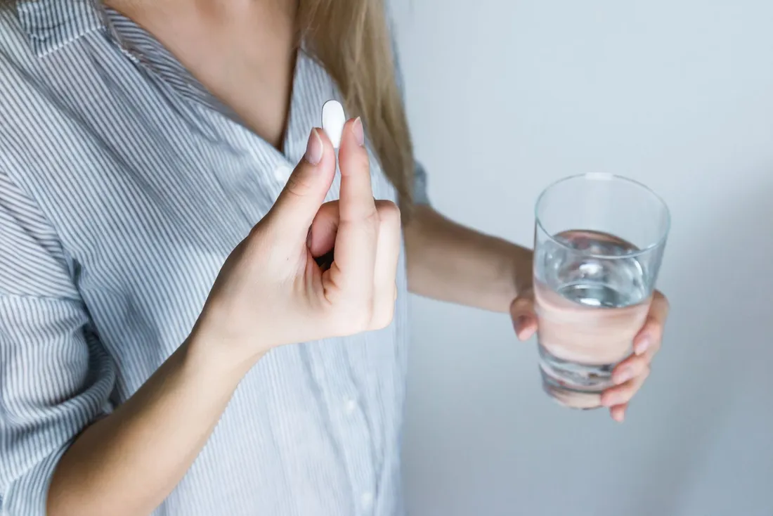 A woman holding a glass of water and a pill