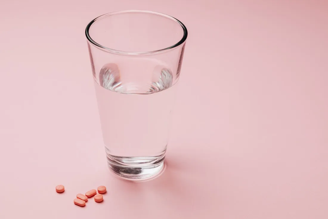 A glass of water next to a bottle of capsules